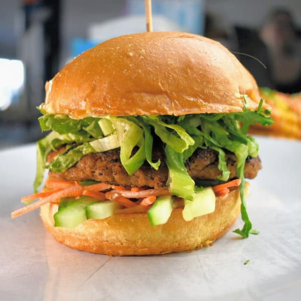 A Lilo's Streetfood burger with a patty, lettuce, shredded carrots, and cucumber on a bun.
