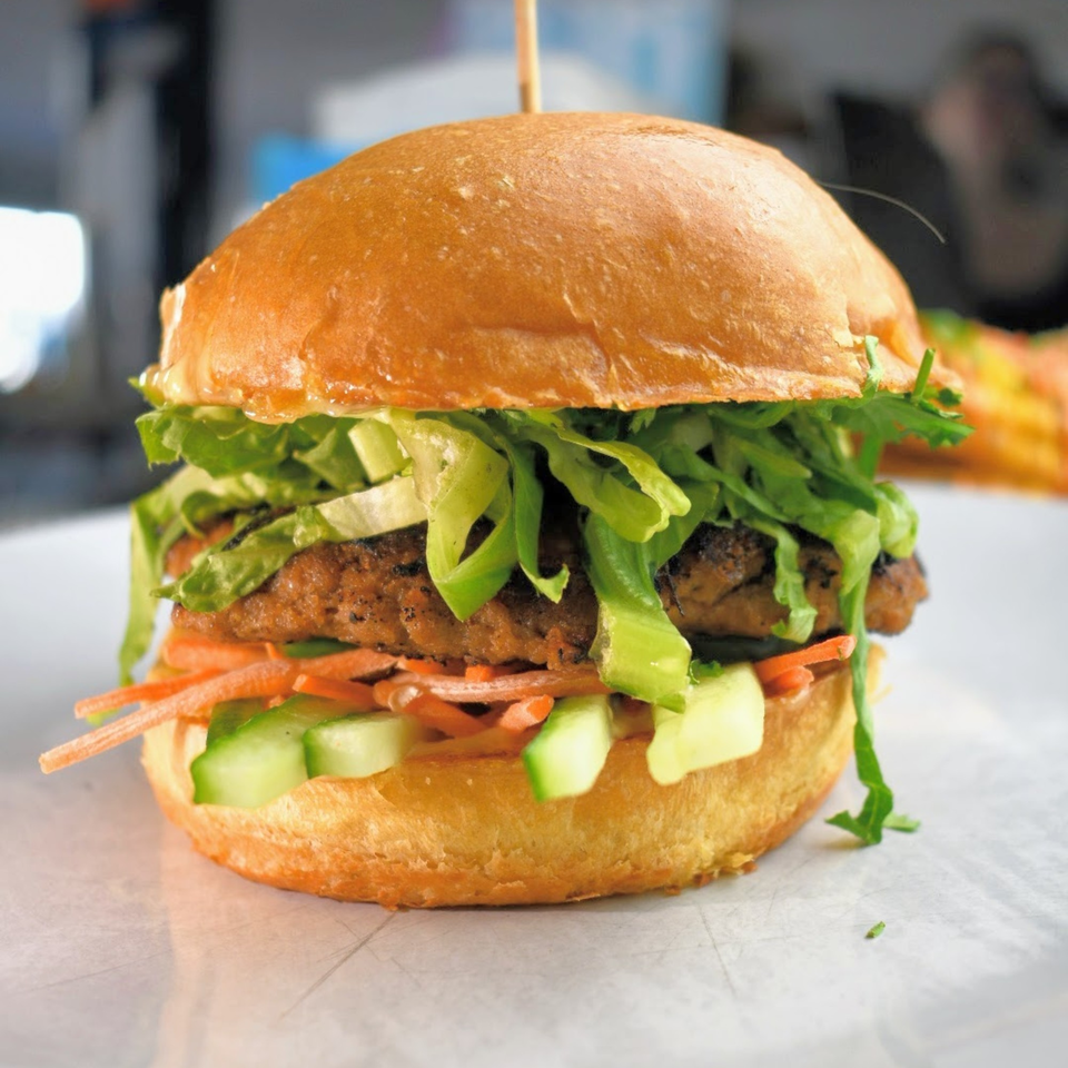 A Lilo's Streetfood burger with a patty, lettuce, shredded carrots, and cucumber on a bun.