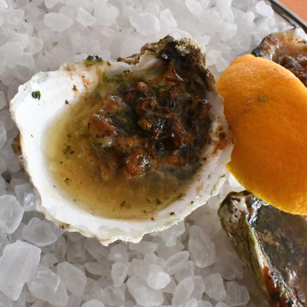 Baked oyster with sauce and a lemon wedge on a bed of crushed ice.