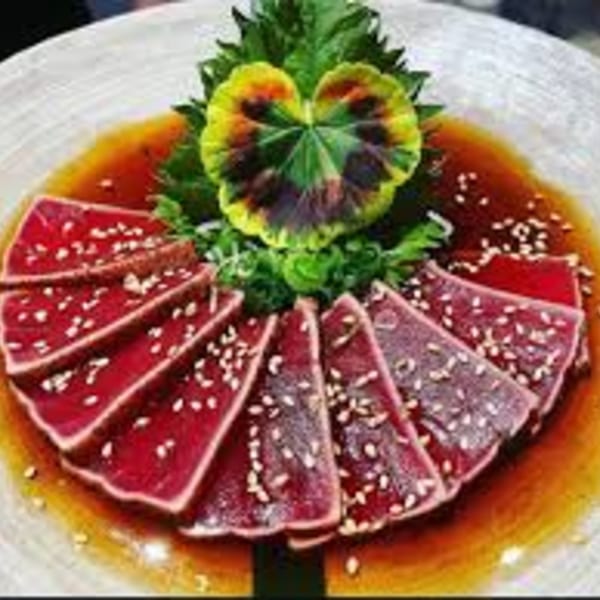 Seared tuna slices with sesame seeds and sauce, garnished with a vibrant green and yellow leaf.