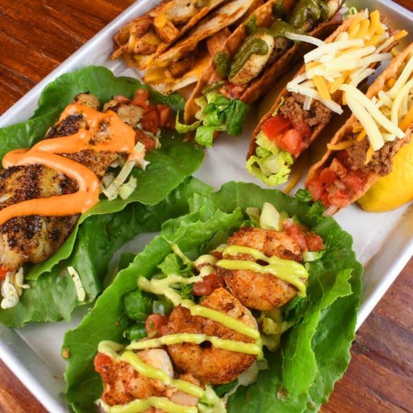 A tray of Lilo's Streetfood tacos and lettuce wraps with various fillings and sauces.