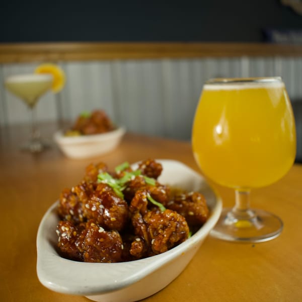 A bowl of Lilo's Streetfood's American-style chicken bites with sesame seeds and a beer.
