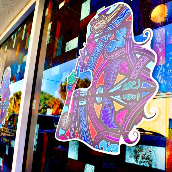 Colorful, patterned silhouette of a person's head and shoulders on a restaurant window with stained glass.