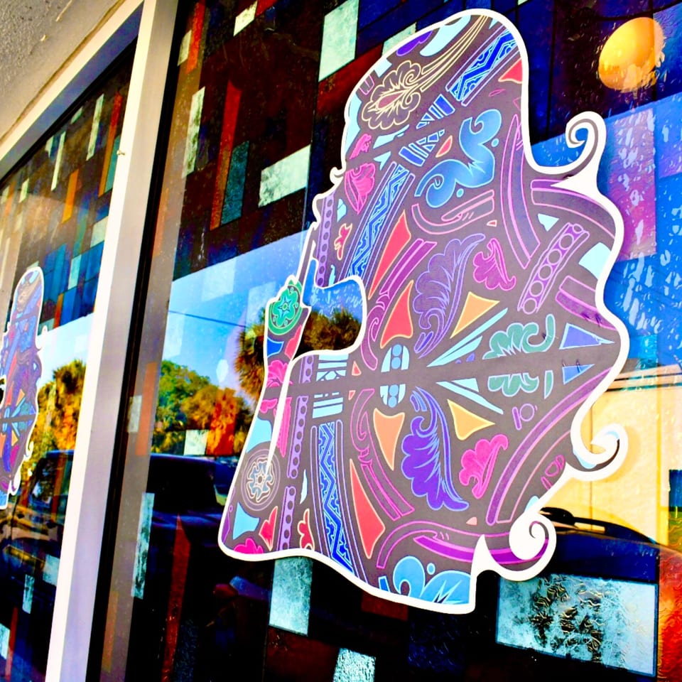 Colorful, patterned silhouette of a person's head and shoulders on a restaurant window with stained glass.