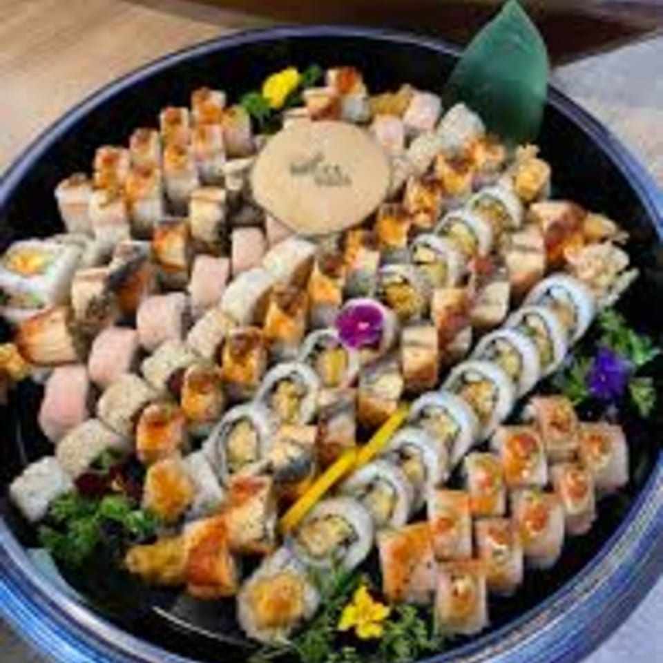 A large platter of various sushi rolls, including maki and nigiri, garnished with flowers and greens.