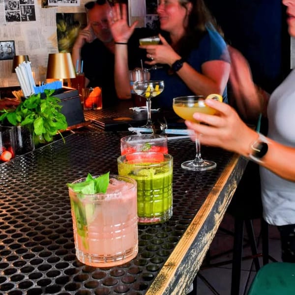 People enjoying colorful cocktails at a lively bar with dim lighting and a textured counter.
