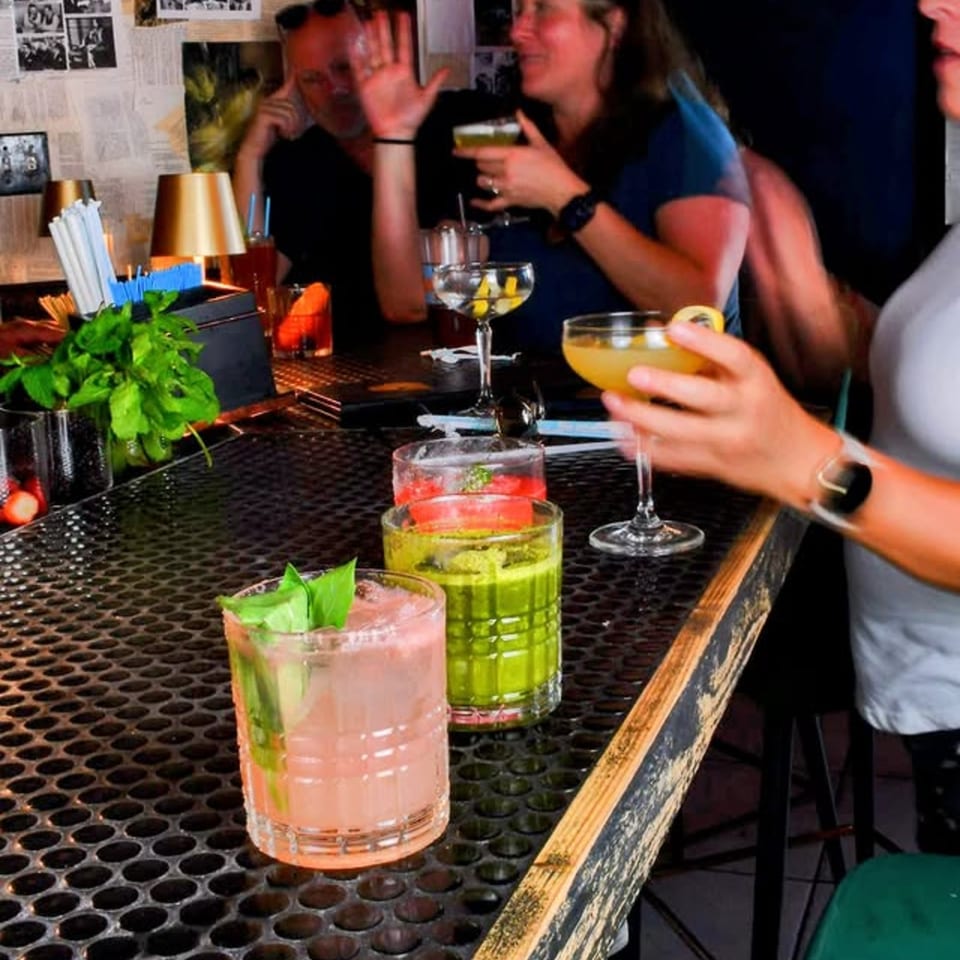 People enjoying colorful cocktails at a lively bar with dim lighting and a textured counter.