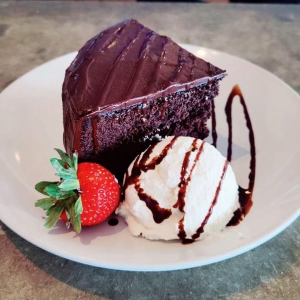 A slice of rich chocolate cake with ice cream, chocolate drizzle, and a fresh strawberry.