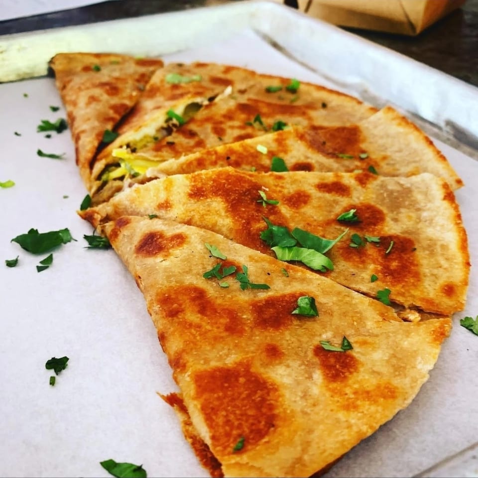 Golden-brown quesadilla slices, garnished with fresh green herbs, on a white serving paper.