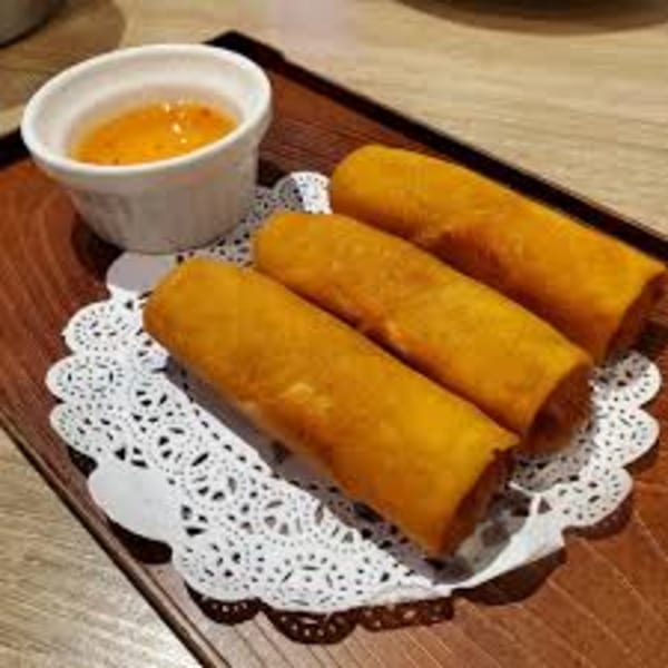 Three golden-brown spring rolls with a side of orange dipping sauce on a wooden tray.