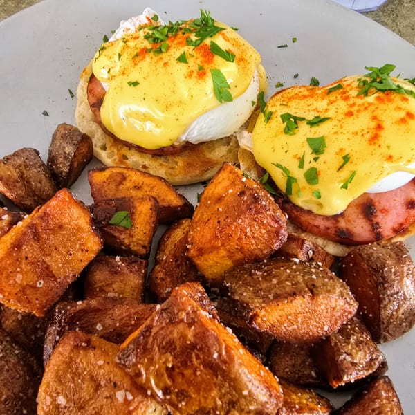Two eggs Benedict with hollandaise sauce, paprika, and parsley, served with crispy roasted potatoes.