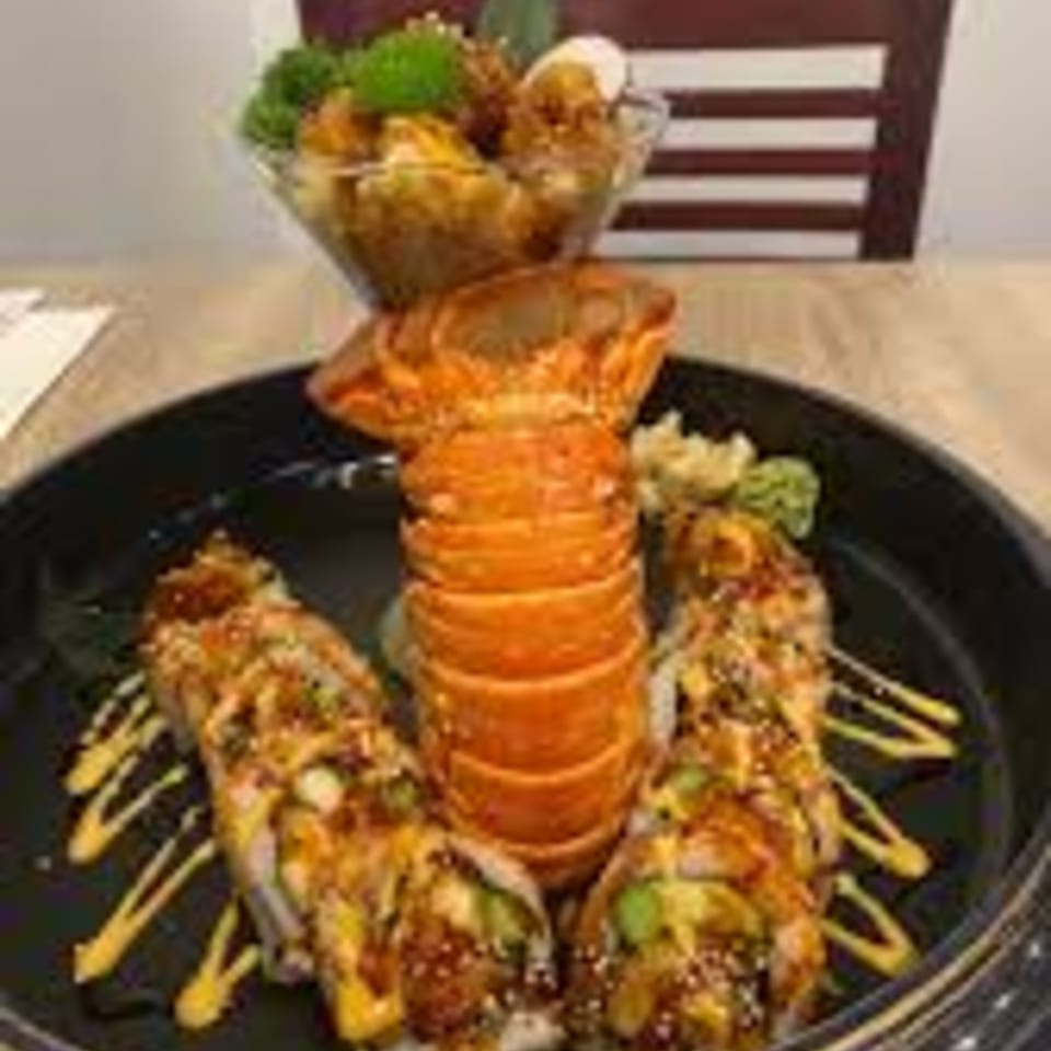 Lilo's Streetfood & OKA Sushi's lobster tail and sushi rolls with sauce, served on a black plate.