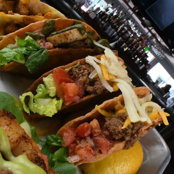 Three American-style tacos with various fillings, including ground beef, lettuce, tomatoes, and cheese, on a plate.