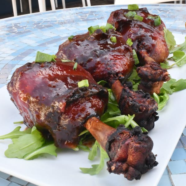 Three American-style chicken lollipops with dark glaze and green onions on a bed of arugula.