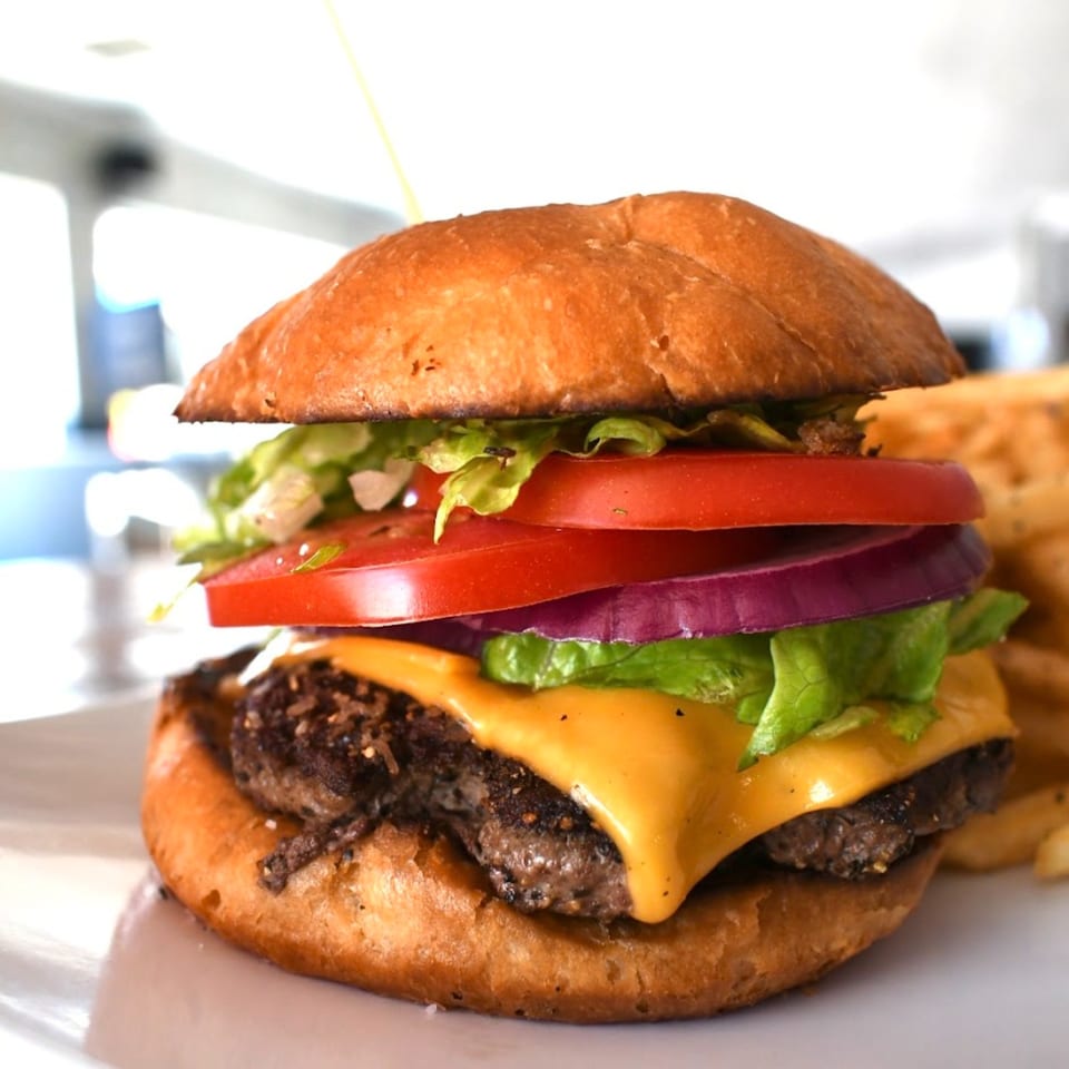 A Lilo's Streetfood cheeseburger with lettuce, tomato, and onion, served with fries.