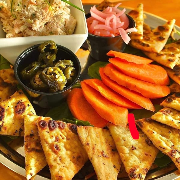A platter with tuna salad, pickled onions, sliced carrots, jalapeños, and flatbread triangles.