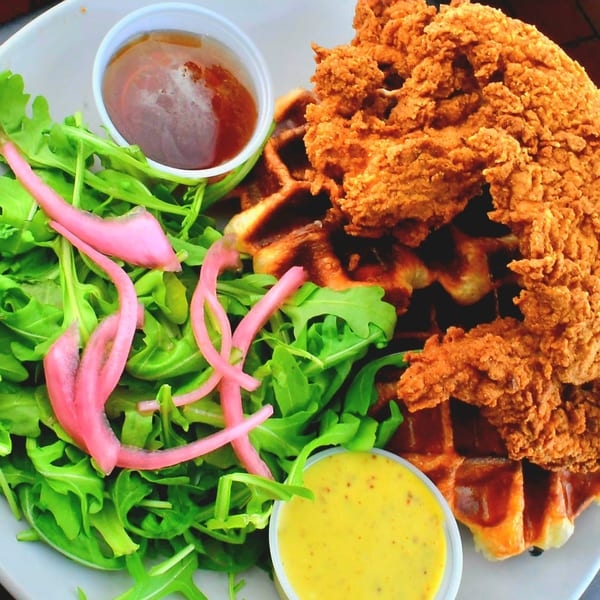 Crispy fried chicken and waffles with a side salad, pickled onions, honey, and mustard sauce.