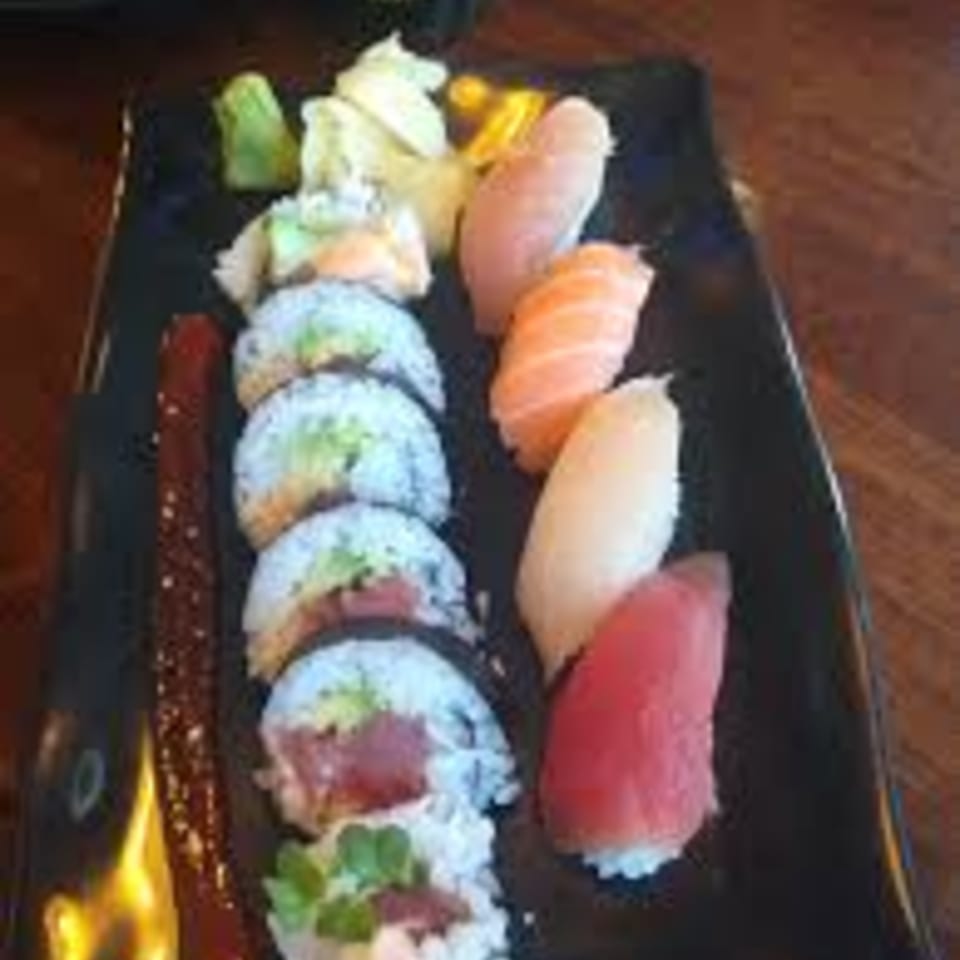A black rectangular plate holds various sushi rolls, nigiri, wasabi, and pickled ginger.