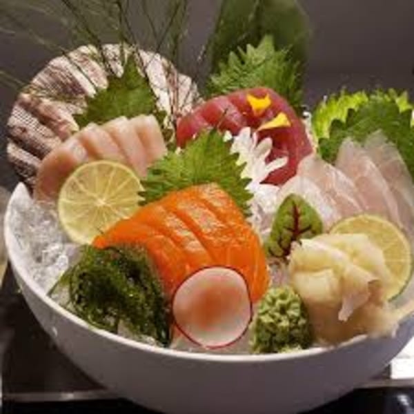 A white bowl filled with various sashimi, seaweed, lime slices, and ginger on ice.